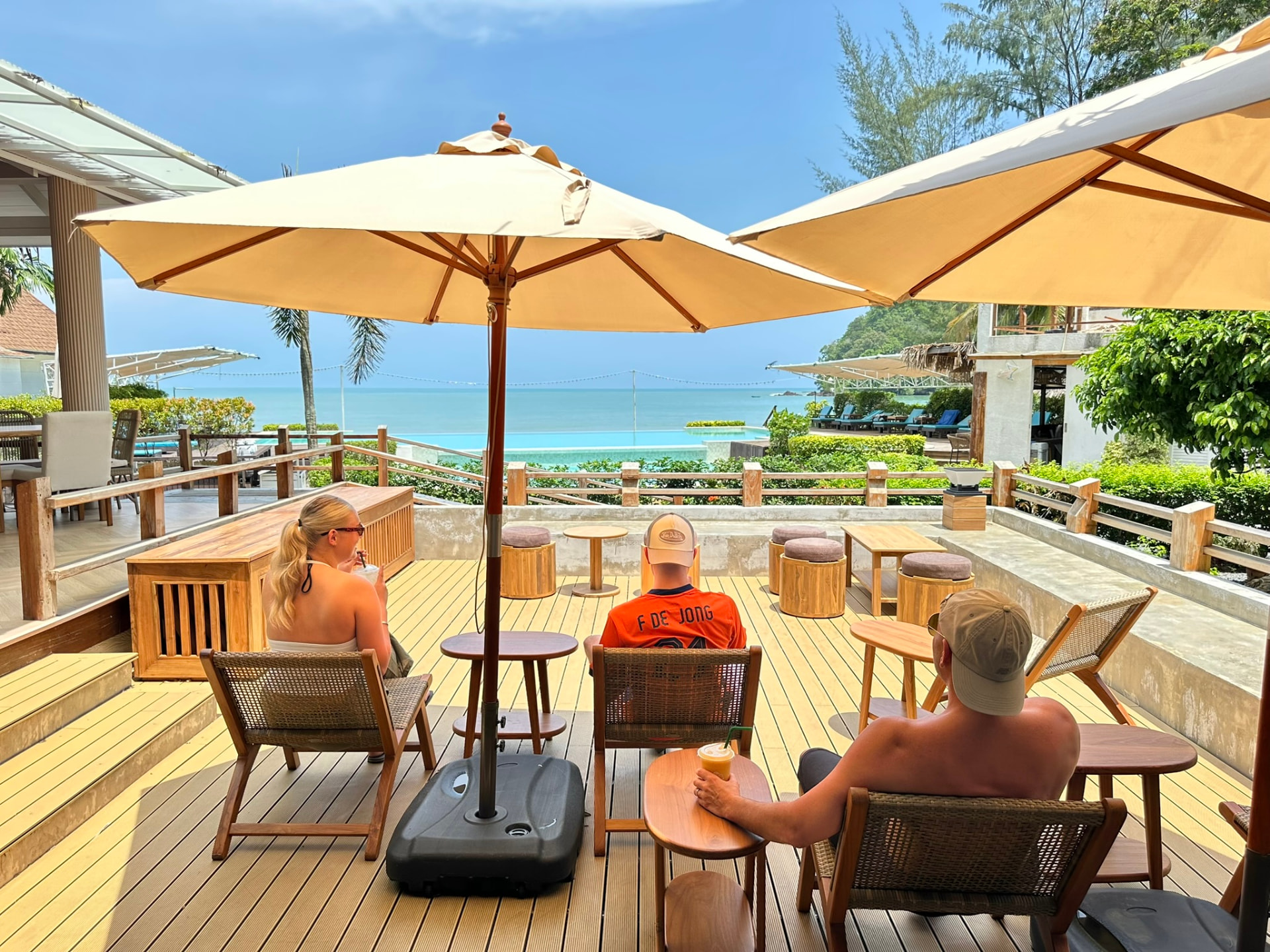 Guests sitting on the shaded deck at Breezy Bites looking out over the pool and sea