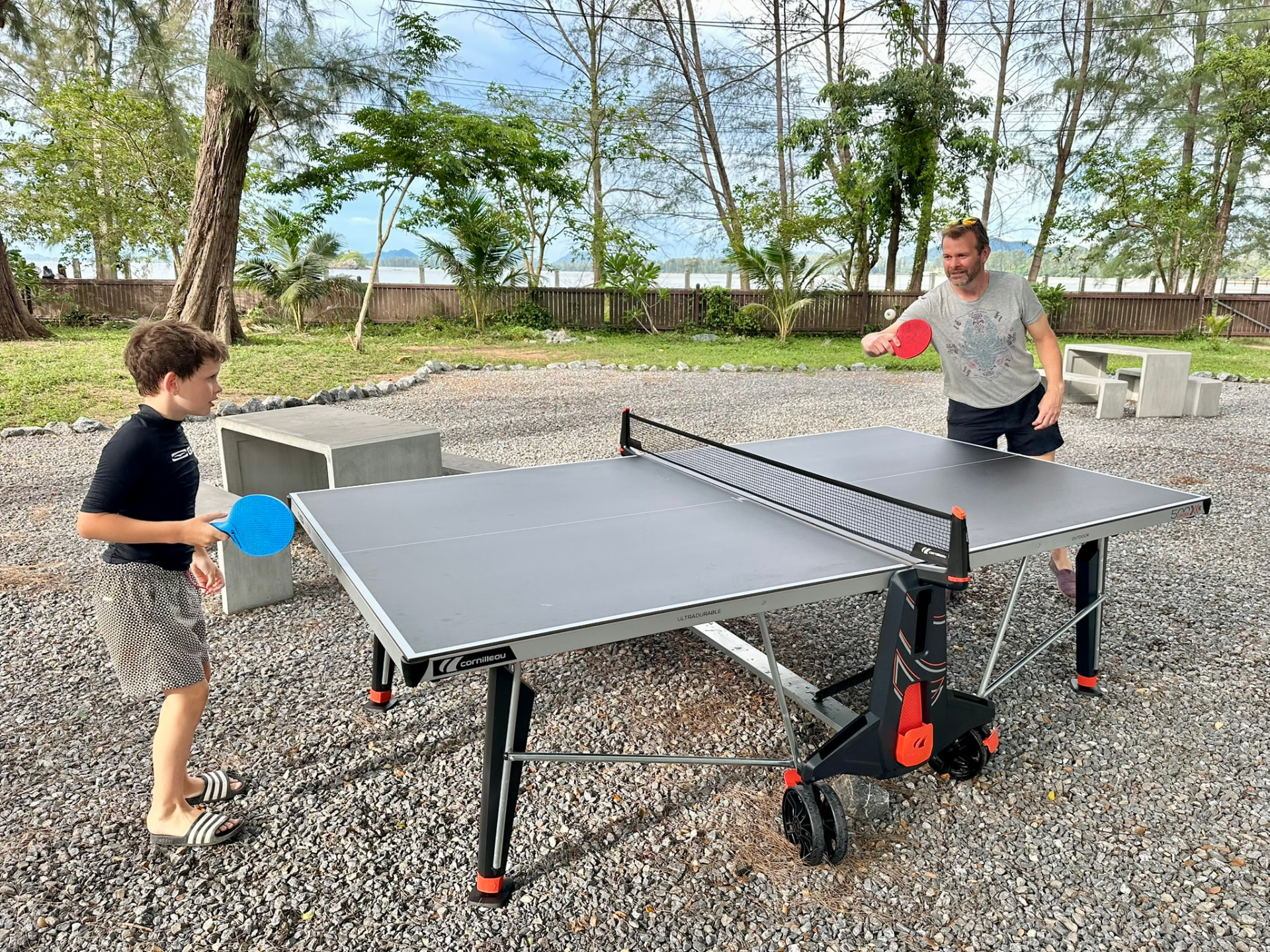 Father and son playing table tennis with the sea behind them