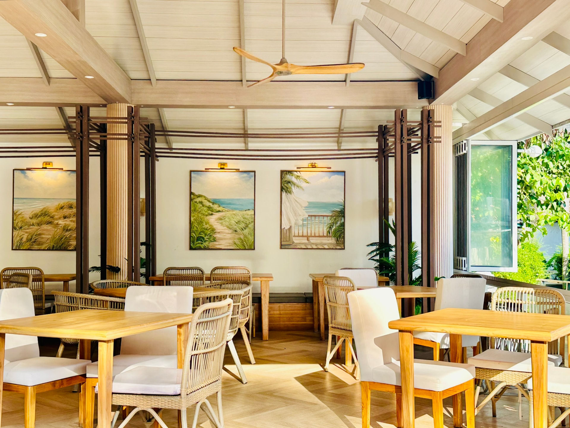Teak tables and rattan chairs beneath the pitched ceiling at Breezy Bites