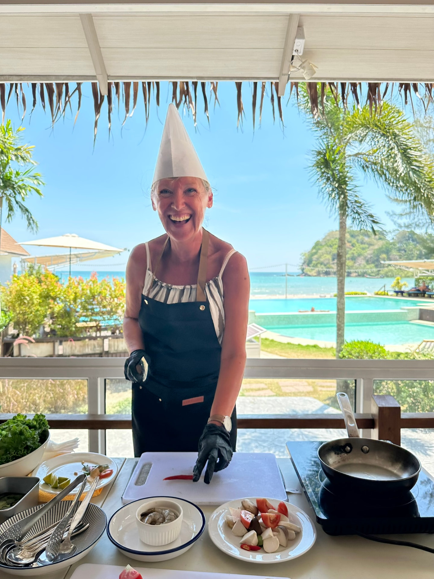 A guest laughing while chopping chilli with the pool and sea behind
