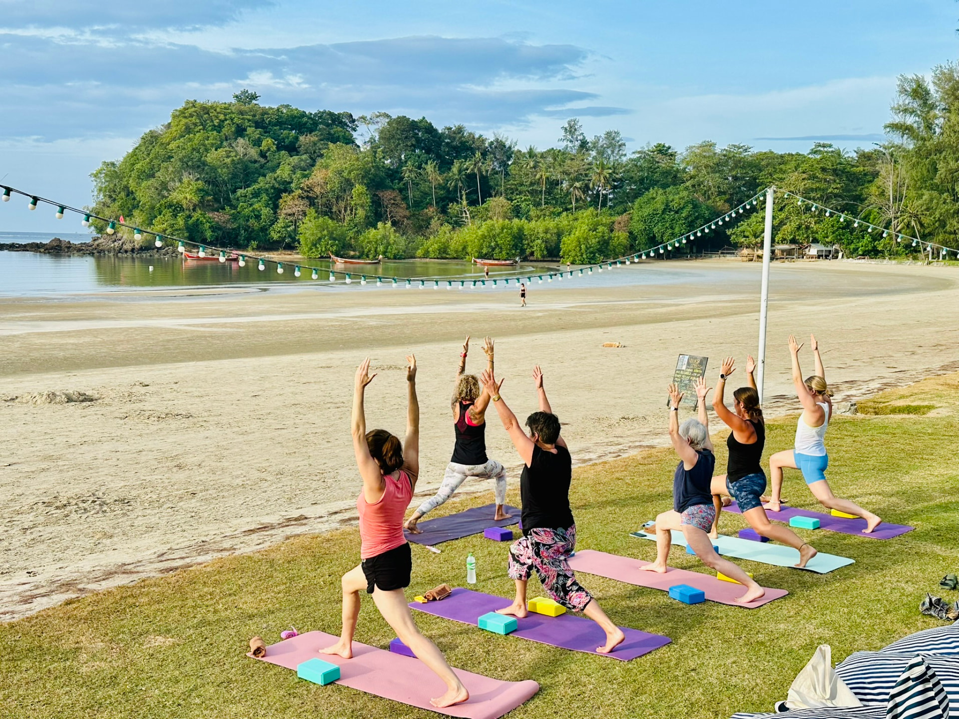 A group yoga class flowing together on the lawn beside the beach