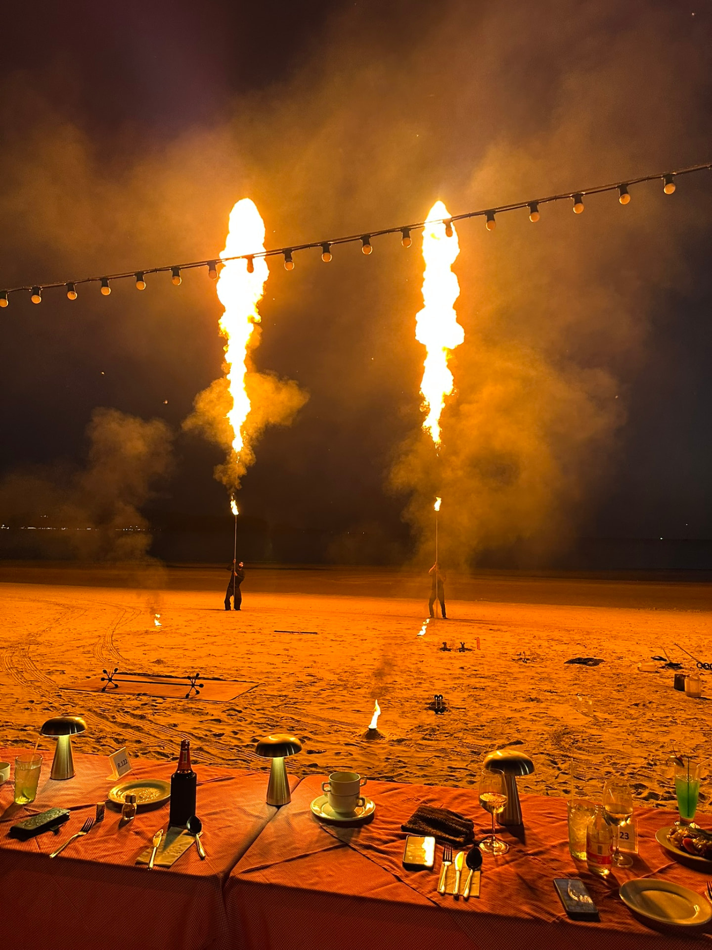 Two performers sending tall columns of flame into the night sky above the beach