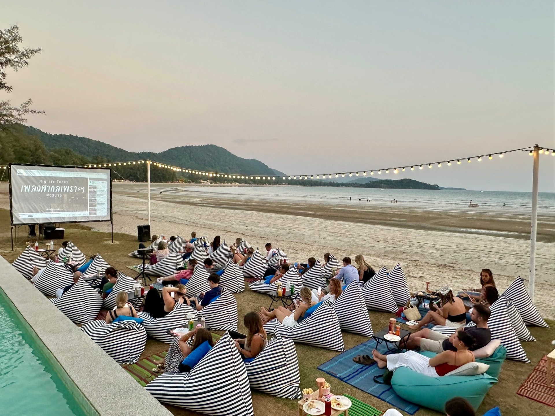 Guests settling onto bean bags at dusk with the beach and hills behind the screen