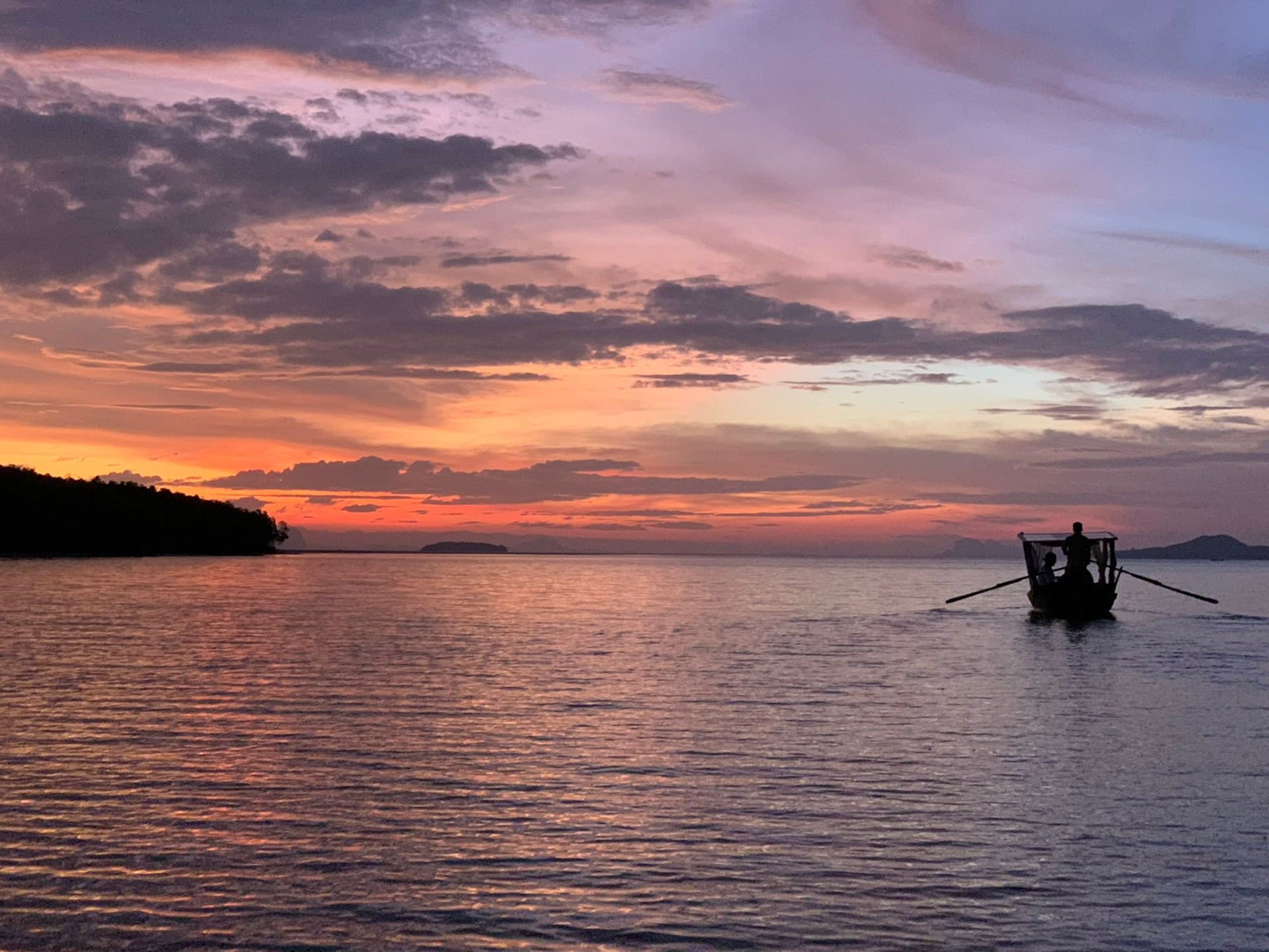 A longtail boat silhouetted against a golden Koh Lanta sunset