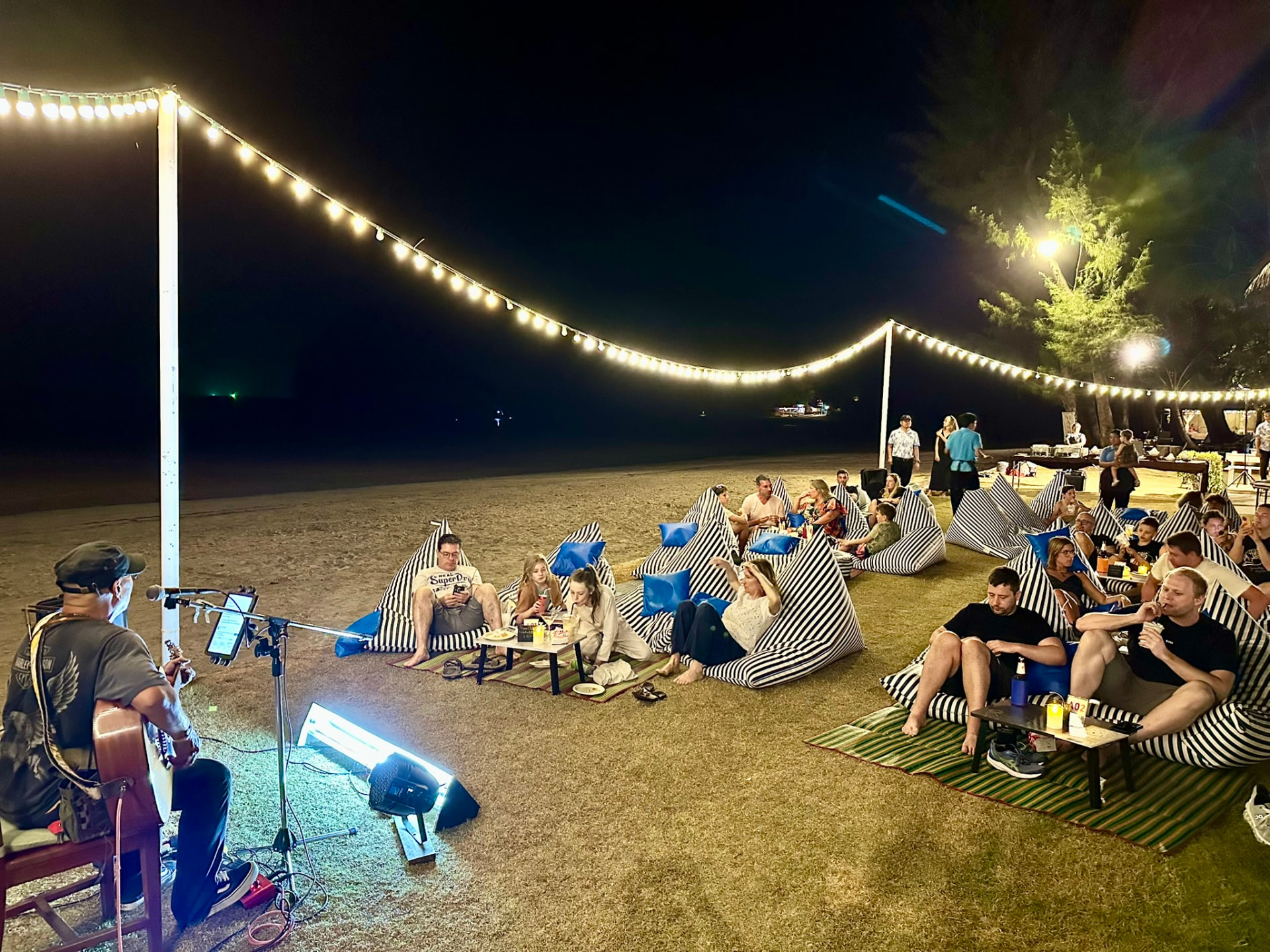 Guests lounging on striped bean bags on the beach listening to a guitarist play