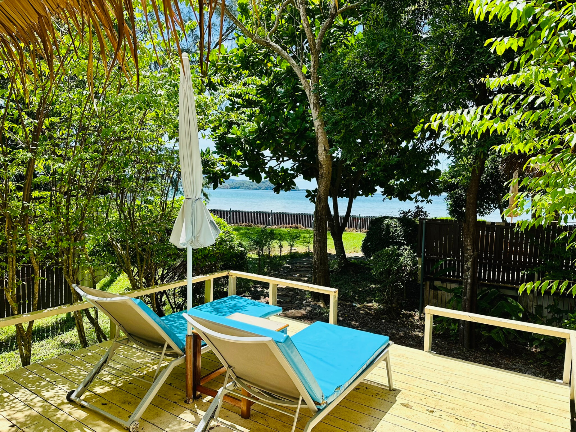Two sunbeds and a parasol on a timber terrace with the bay visible through the trees