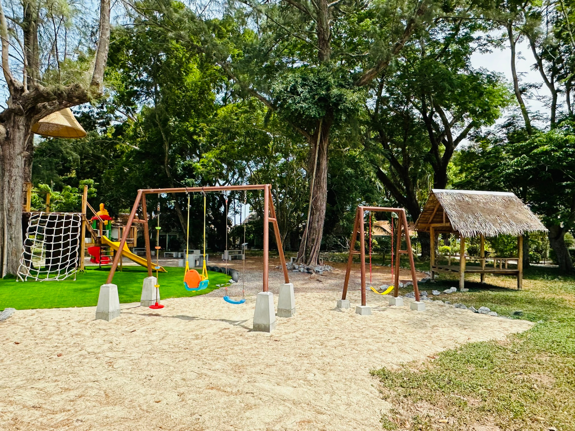 Swing sets on the sand next to the lawn and a thatched sala